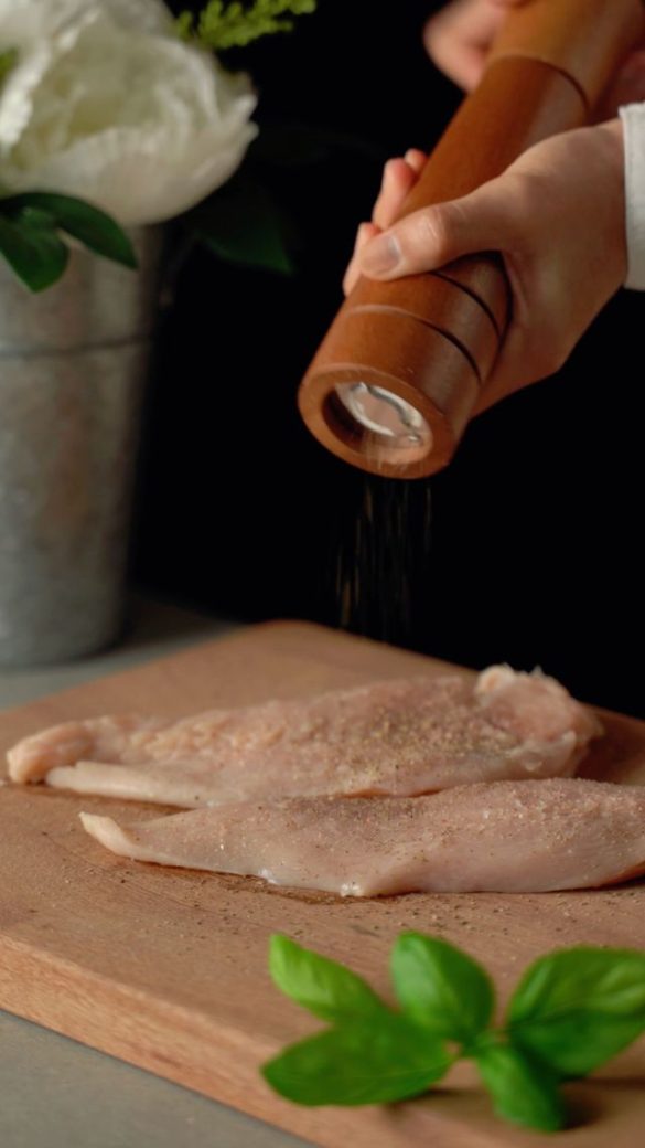 Handen die rauwe kipfilet kruiden op een houten snijplank